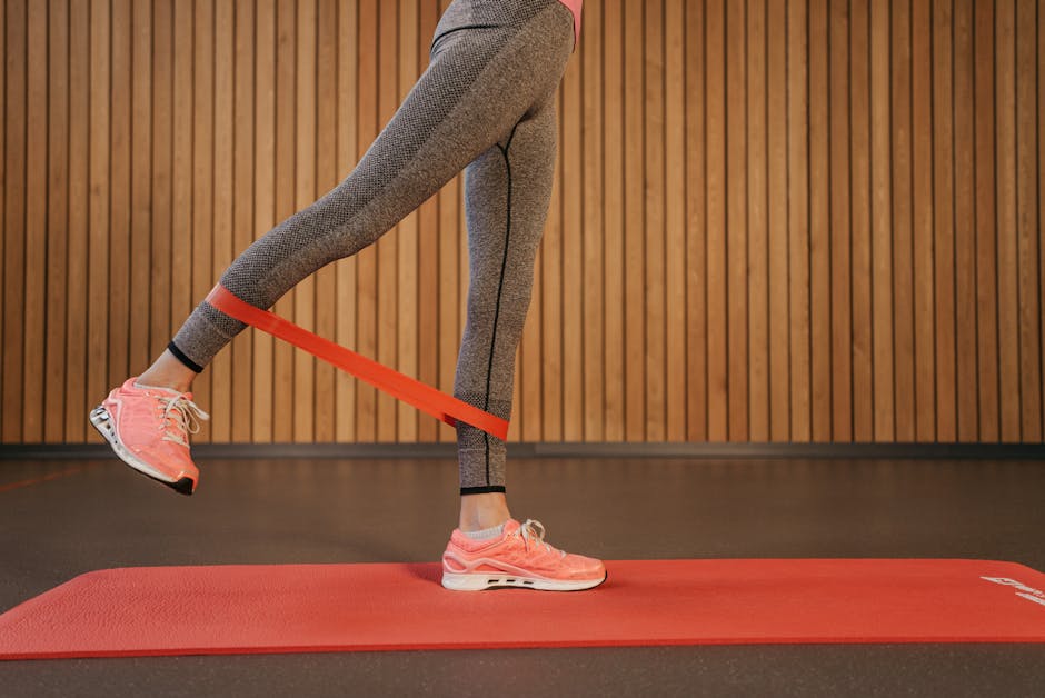 A woman performing leg exercises using a red resistance band on a yoga mat indoors